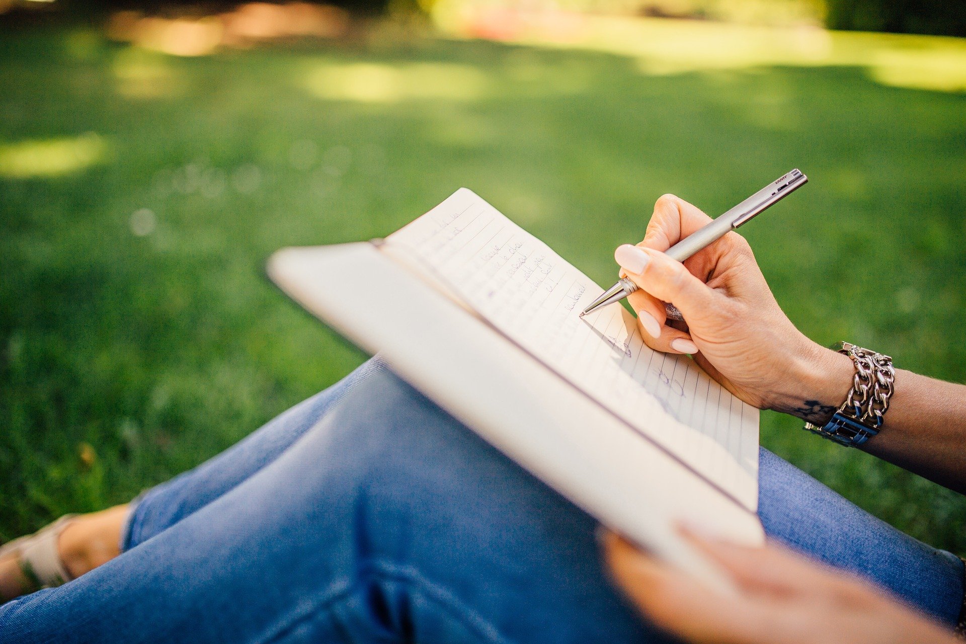 girl who is sitting on the grass and writing in the notebook